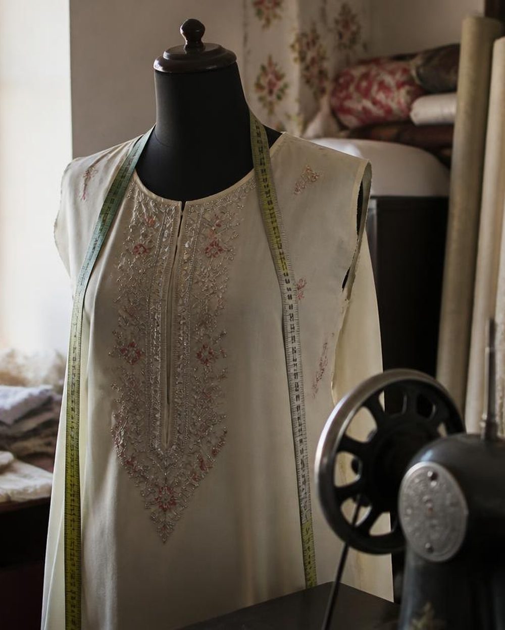 Embroidered ladies suit on a dress form beside fabric rolls in the tailoring workroom