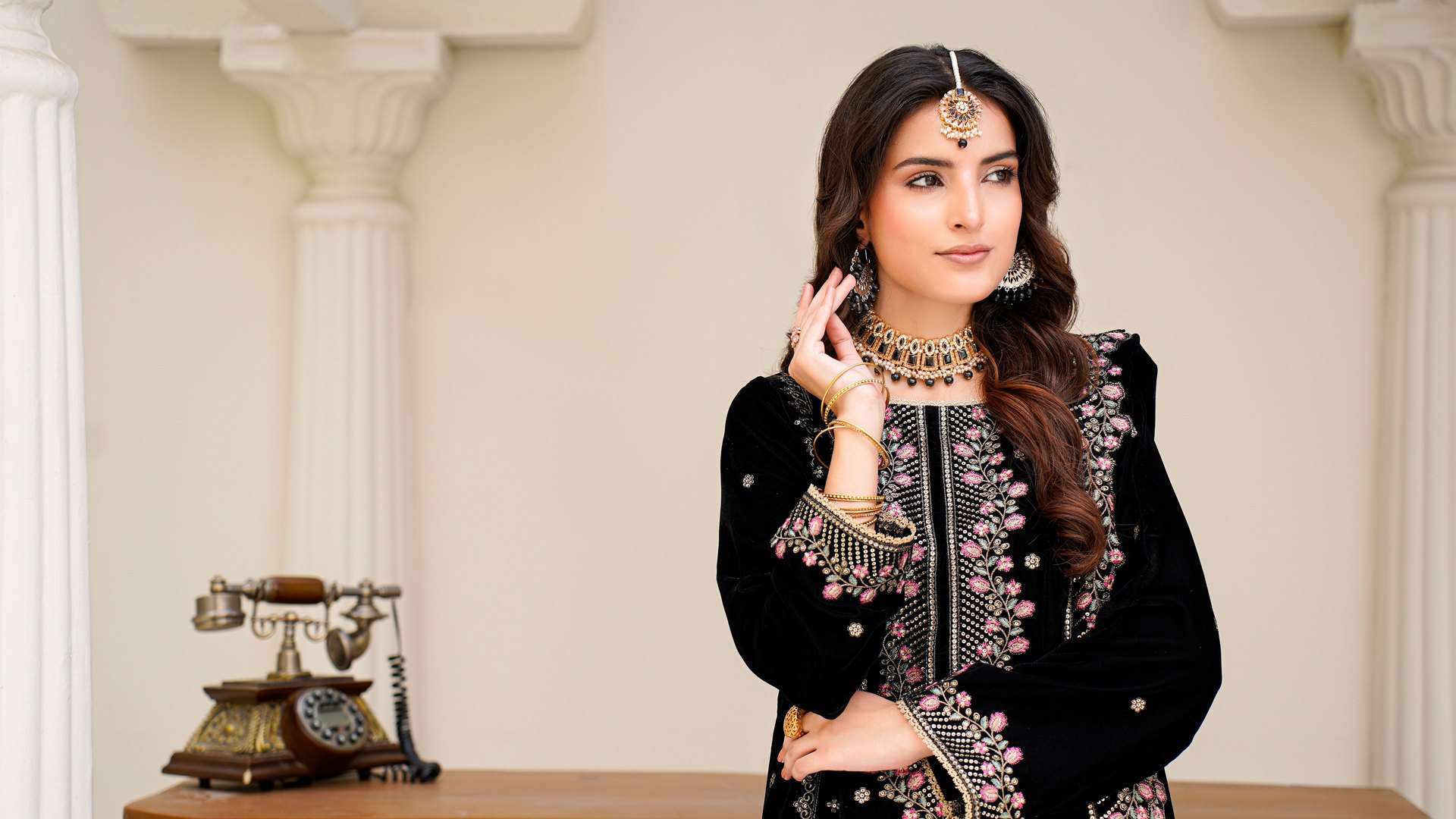 Black velvet Pakistani ladies suit with pink and gold embroidery, styled in a soft studio setting